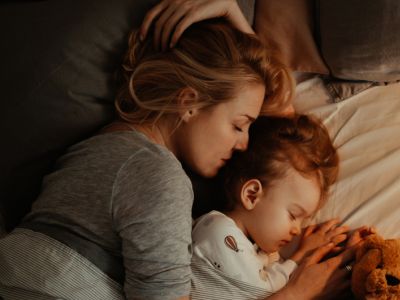 Eine Mutter und ihre Tochter kuscheln im Bett; Positive Erziehung kann Kindern helfen, Schlafprobleme zu überwinden.