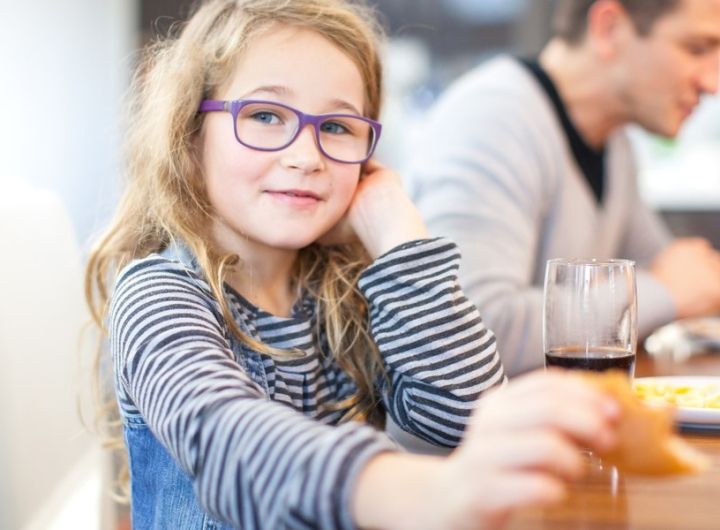 girl wearigng glasses looks at camera as she enjoys a meal with the family