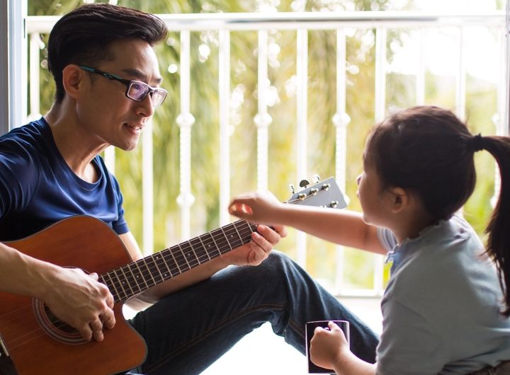 Dad plays guitar as child points to frets